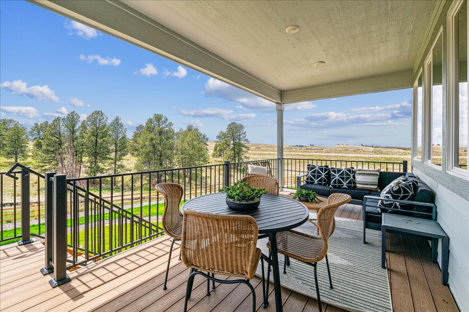 A deck with a table and chairs on it and trees in the background.