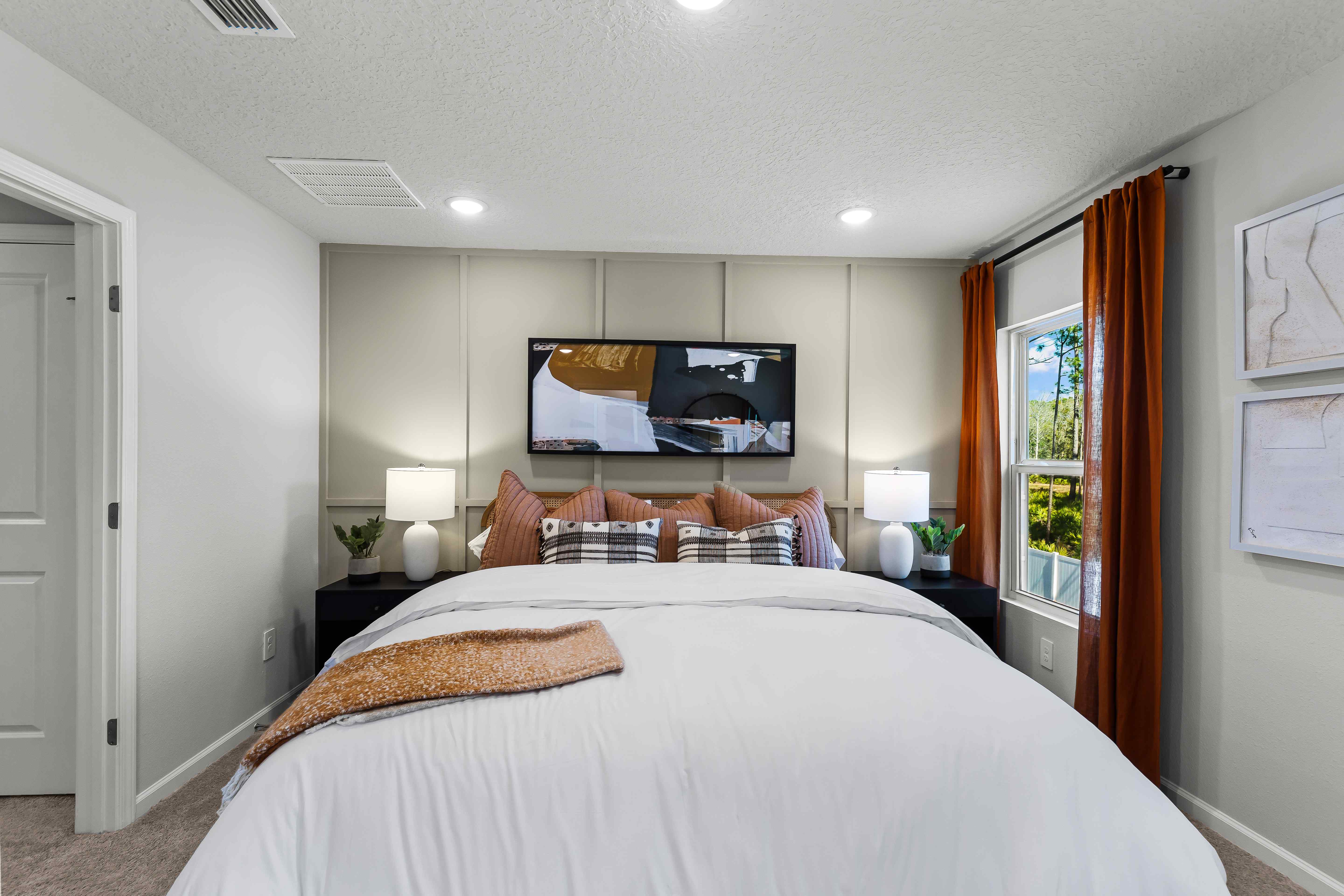 Davor Model Paired Home Primary Bedroom with Orange Bed Comforter and Pillows in Front of Cream Accent Wall at The Landings at Pecan Park