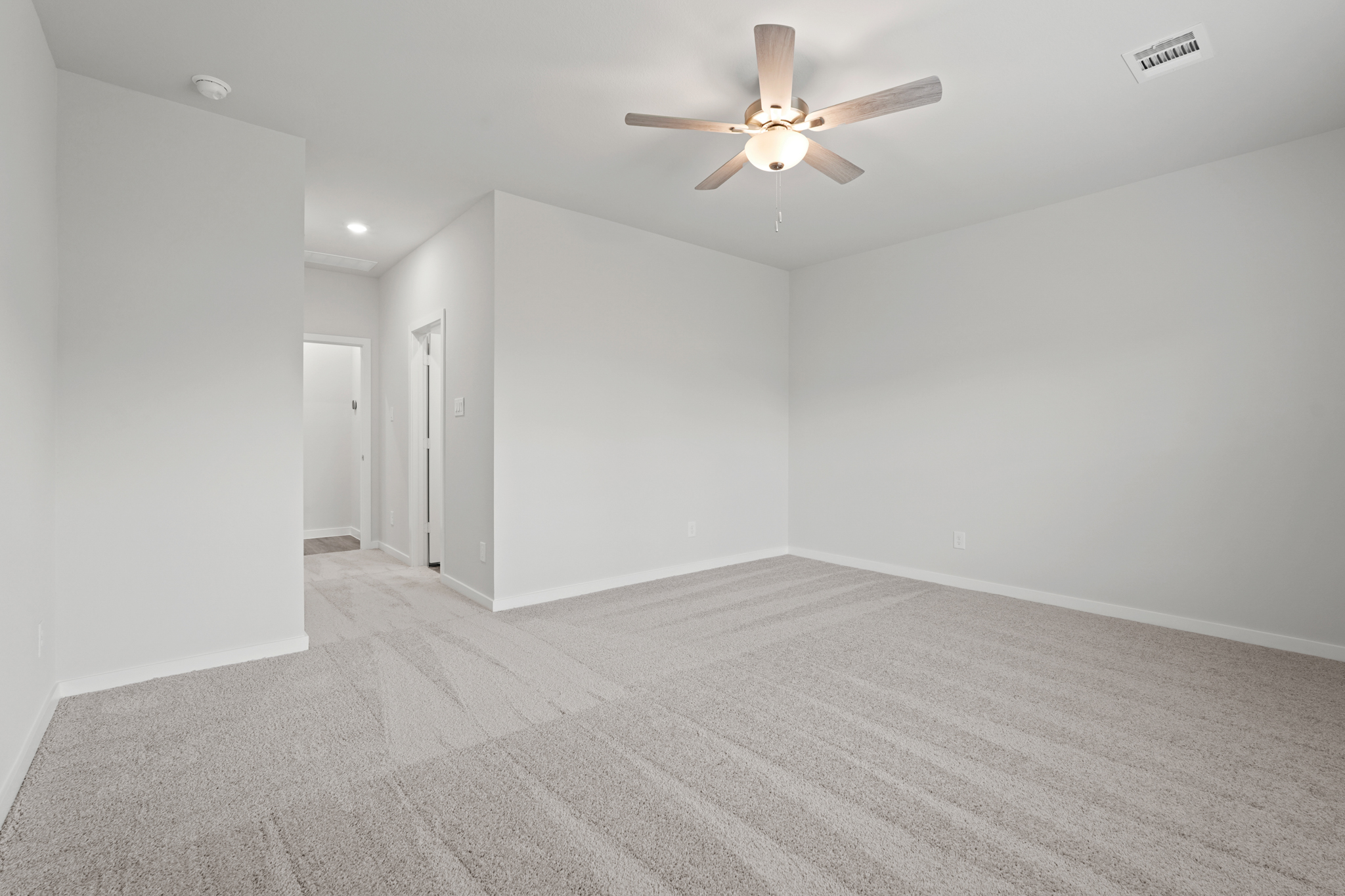 A room with a ceiling fan and a carpet.